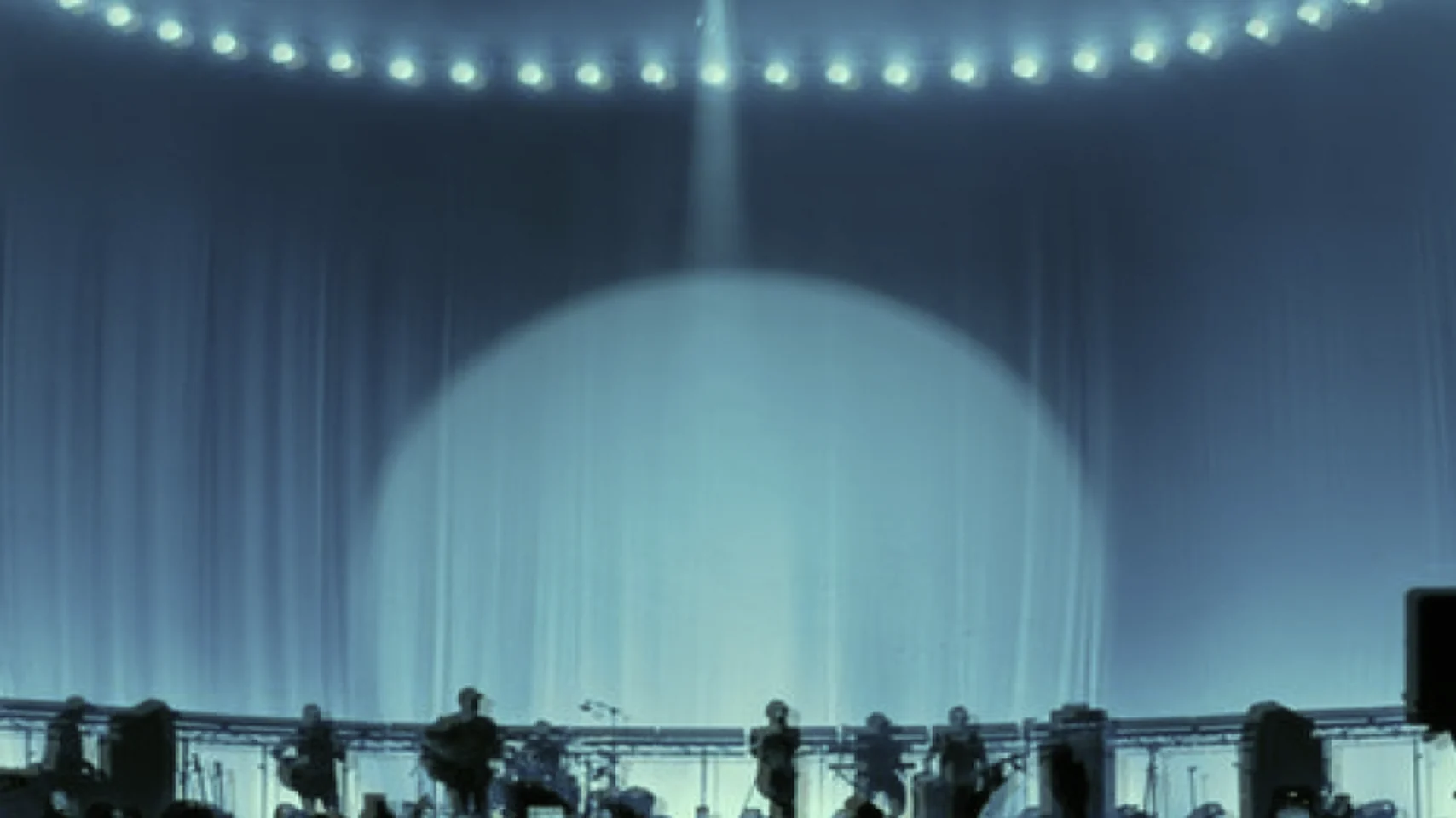 A stage under a single spotlight, orchestra silhouetted against a lit scrim