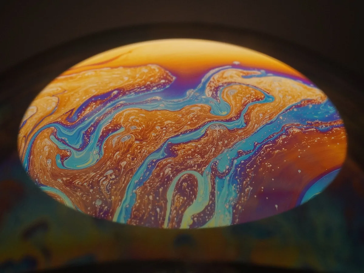 Bands of cyan, amber, violet, and white produced by thin-film interference on a soap bubble